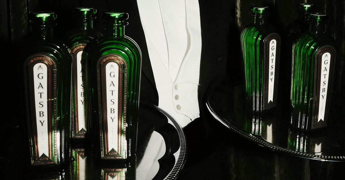 Bottles of Gatsby Gin on two silver trays, carried by a waiter in evening dress.