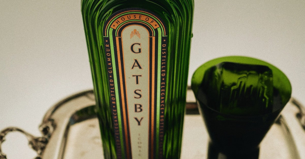 A bottle of Gatsby Gin beside a green coupe glass on a silver tray.