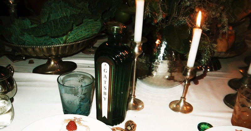 A bottle of Gatsby Gin on a candlelit dinner table after the meal, beside a glass and silver candlesticks.