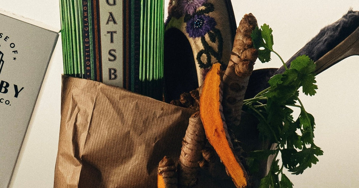 Fresh turmeric root, sliced to show its orange interior, with coriander leaf and a bottle of Gatsby Gin in a paper market bag.