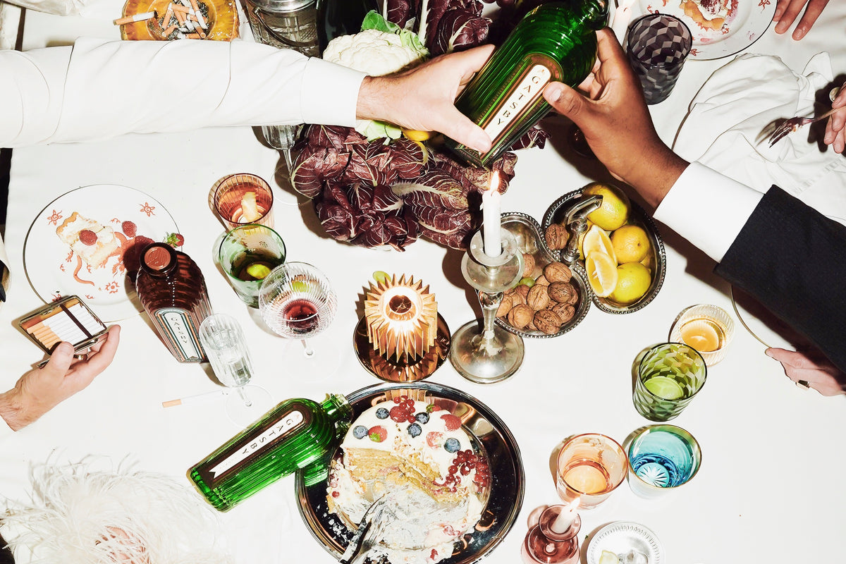 An overhead view of a crowded dinner table with bottles of Gatsby Gin being passed between guests